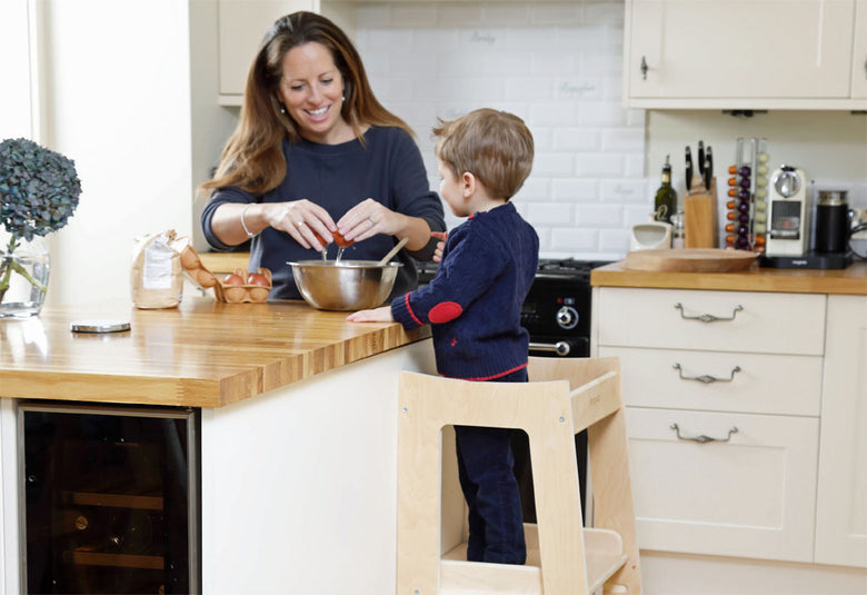 Mixing ingredients to bake cake in kitchen helper. 18 month old baby helping in the kitchen in learning tower.